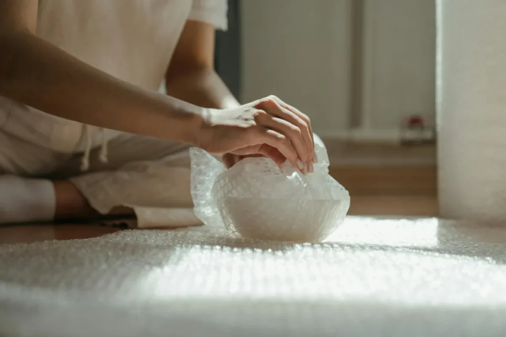 Tangan sedang membungkus barang dengan bubble wrap untuk perlindungan pengiriman